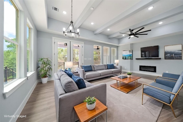 living room featuring beamed ceiling, ceiling fan with notable chandelier, and light hardwood / wood-style floors