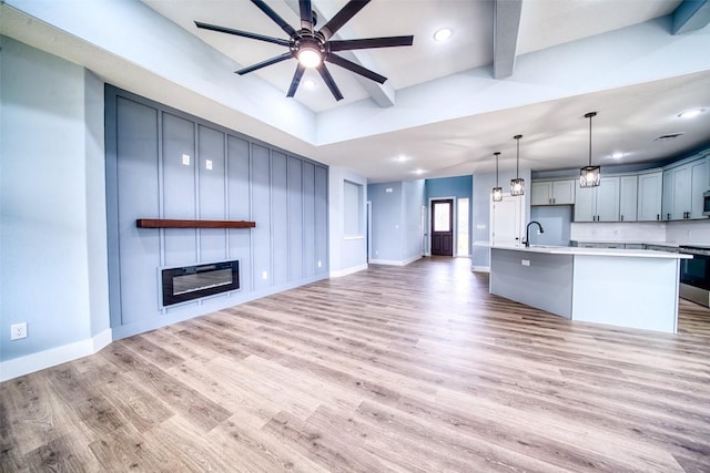 unfurnished living room featuring beamed ceiling, a large fireplace, sink, ceiling fan, and light wood-type flooring