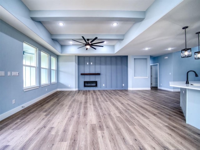 unfurnished living room featuring sink, light wood-type flooring, a large fireplace, beamed ceiling, and ceiling fan