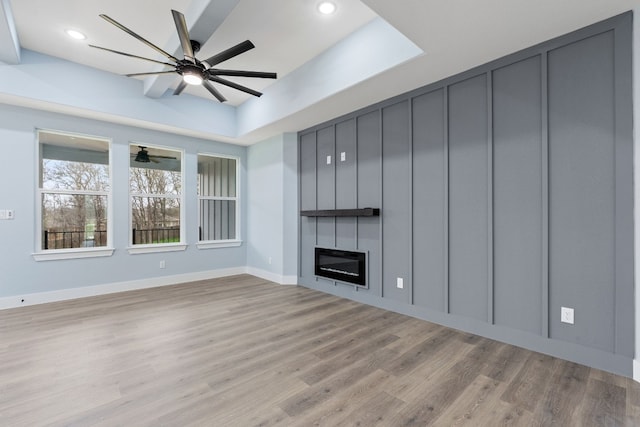 unfurnished living room with ceiling fan, a tray ceiling, a fireplace, and light hardwood / wood-style floors