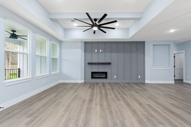 unfurnished living room featuring beamed ceiling, a large fireplace, ceiling fan, and light wood-type flooring