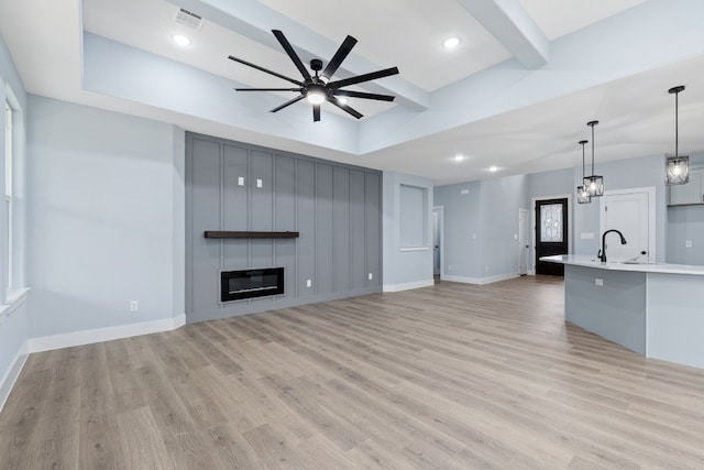 unfurnished living room featuring a fireplace, sink, light hardwood / wood-style flooring, ceiling fan, and beam ceiling