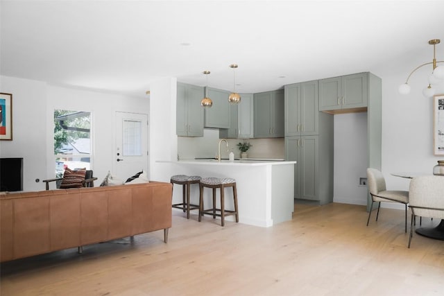 kitchen featuring decorative light fixtures, sink, a kitchen breakfast bar, light hardwood / wood-style floors, and kitchen peninsula