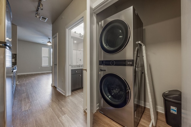 clothes washing area with ceiling fan, stacked washer / dryer, rail lighting, and light wood-type flooring