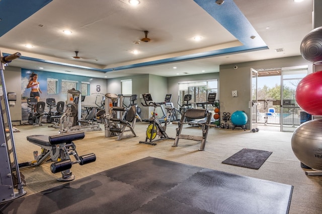 gym featuring carpet floors, ceiling fan, and a tray ceiling