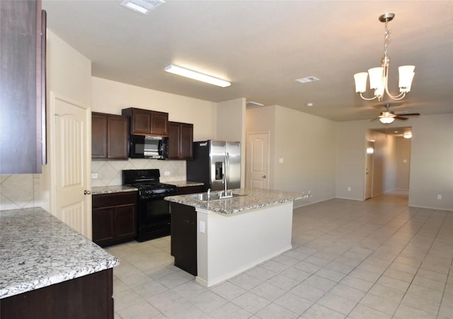 kitchen with ceiling fan with notable chandelier, a kitchen island with sink, light stone countertops, black appliances, and decorative light fixtures