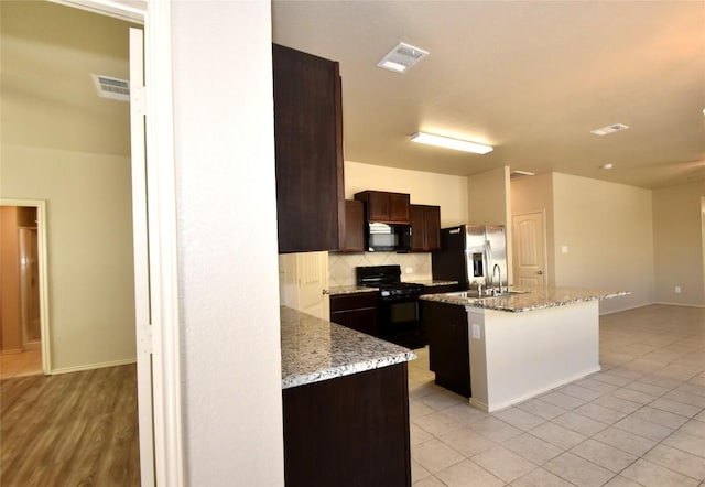 kitchen featuring decorative backsplash, a center island, dark brown cabinetry, black appliances, and light stone countertops