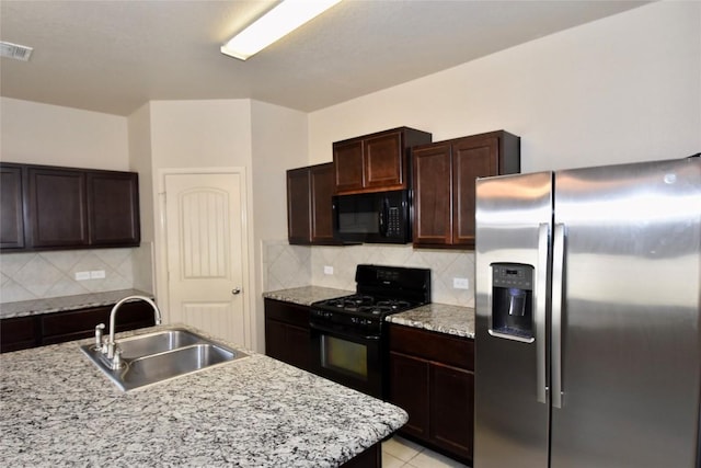 kitchen featuring sink, light stone counters, black appliances, a center island with sink, and backsplash