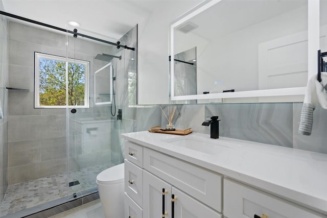 bathroom featuring vanity, decorative backsplash, a shower with door, and toilet