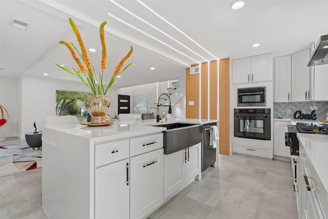 kitchen with sink, white cabinets, backsplash, stainless steel dishwasher, and a center island with sink