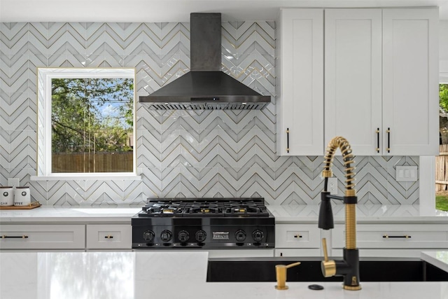 kitchen with tasteful backsplash, gas stovetop, light stone countertops, white cabinets, and wall chimney exhaust hood