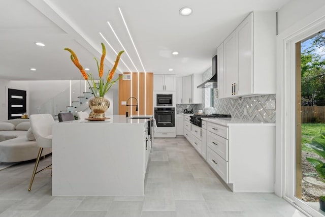 kitchen with black oven, white cabinetry, a center island with sink, built in microwave, and wall chimney exhaust hood