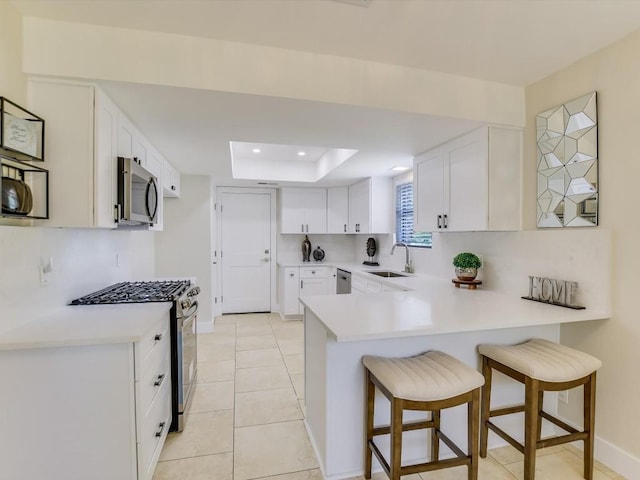 kitchen featuring sink, stainless steel appliances, a kitchen breakfast bar, a tray ceiling, and white cabinets