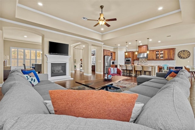 living room featuring a raised ceiling, crown molding, hardwood / wood-style floors, and ceiling fan