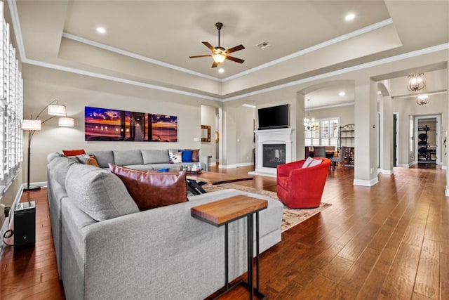 living room featuring ornamental molding, dark hardwood / wood-style floors, ceiling fan with notable chandelier, and a tray ceiling