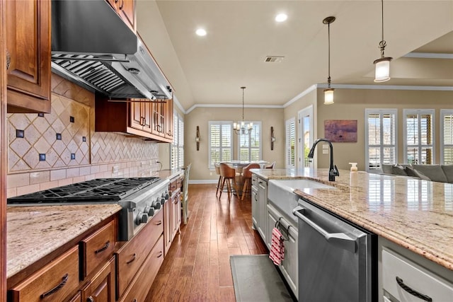 kitchen with dark wood-type flooring, extractor fan, appliances with stainless steel finishes, pendant lighting, and light stone countertops