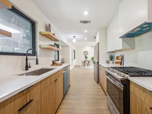 kitchen featuring white cabinetry, sink, backsplash, light hardwood / wood-style floors, and stainless steel appliances