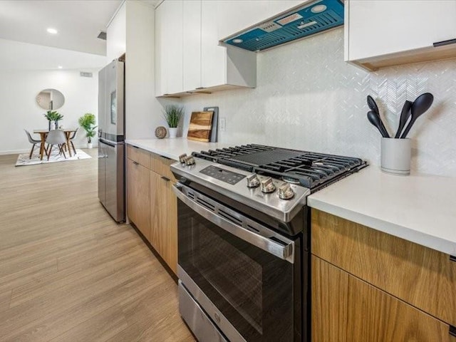 kitchen with extractor fan, white cabinetry, backsplash, light hardwood / wood-style floors, and stainless steel appliances