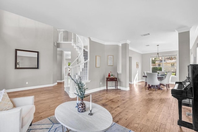 living room featuring a notable chandelier, baseboards, ornamental molding, stairway, and light wood-type flooring