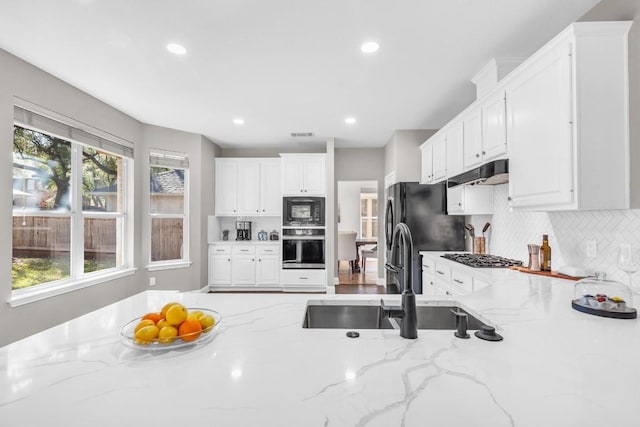 kitchen featuring light stone countertops, under cabinet range hood, black appliances, white cabinetry, and a sink