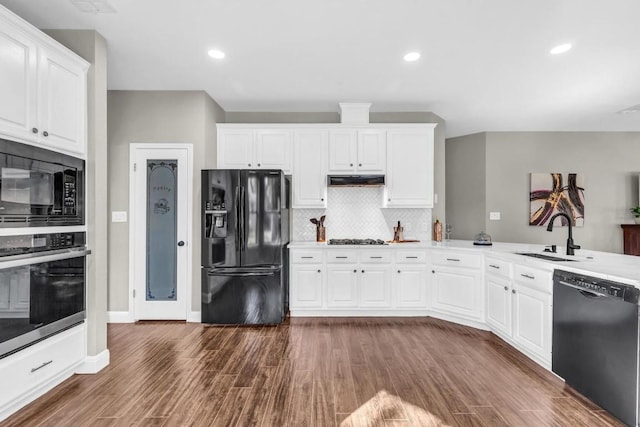 kitchen with dark wood-type flooring, a sink, white cabinets, black appliances, and tasteful backsplash