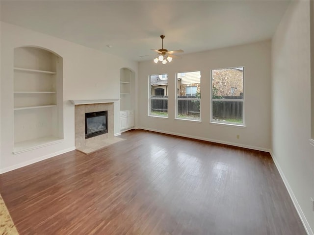 unfurnished living room with dark hardwood / wood-style flooring, a fireplace, built in features, and ceiling fan