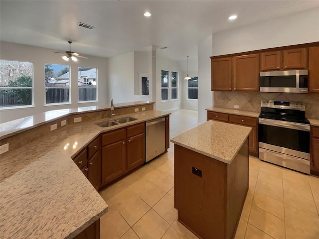 kitchen featuring sink, appliances with stainless steel finishes, a kitchen island, light stone countertops, and backsplash