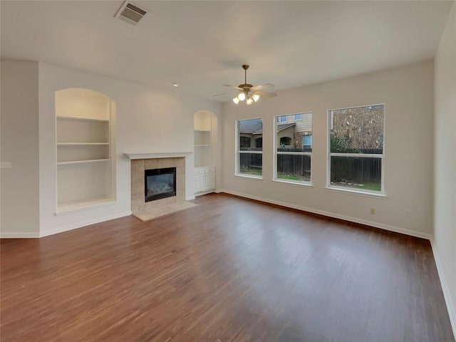 unfurnished living room with a tile fireplace, dark wood-type flooring, built in features, and ceiling fan