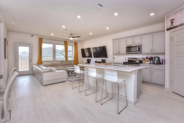 kitchen with gray cabinetry, a sink, open floor plan, stainless steel appliances, and a breakfast bar area