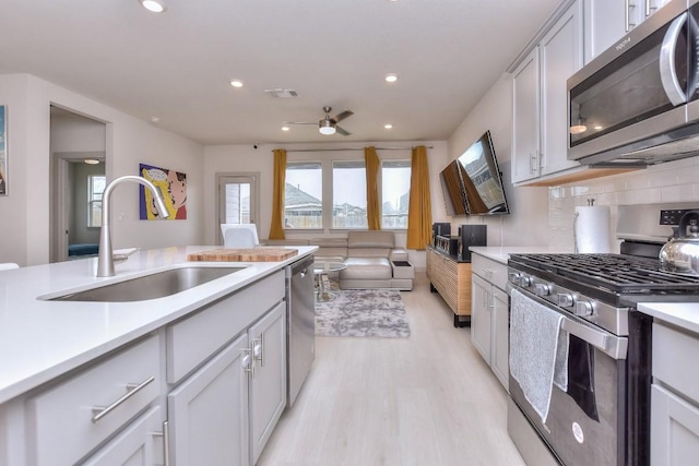 kitchen with sink, decorative backsplash, ceiling fan, light hardwood / wood-style floors, and stainless steel appliances