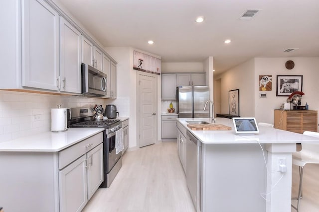 kitchen with tasteful backsplash, gray cabinets, a kitchen island with sink, stainless steel appliances, and light hardwood / wood-style floors