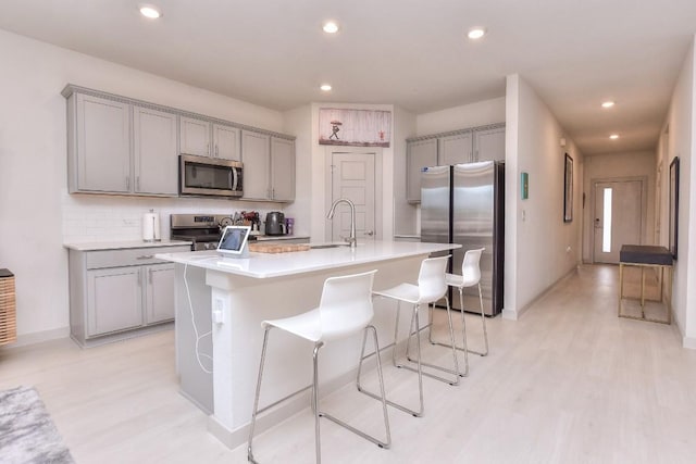 kitchen with gray cabinets, appliances with stainless steel finishes, a breakfast bar, and a center island with sink