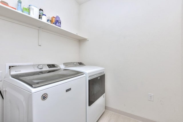 clothes washing area featuring light wood finished floors, laundry area, baseboards, and separate washer and dryer