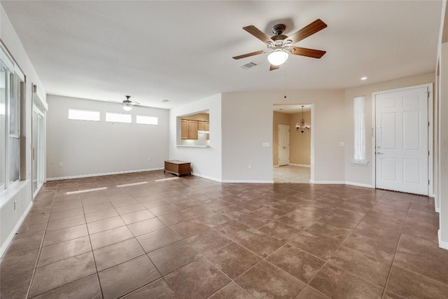 unfurnished living room with ceiling fan with notable chandelier and dark tile patterned floors