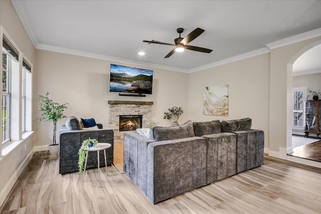 living room featuring crown molding, ceiling fan, a stone fireplace, and light wood-type flooring