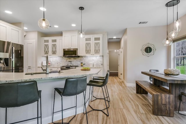 kitchen featuring pendant lighting, stainless steel appliances, tasteful backsplash, light stone countertops, and white cabinets