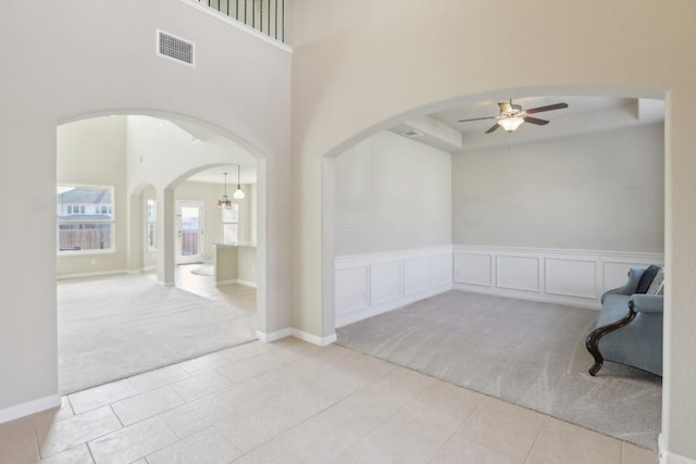 carpeted empty room featuring a raised ceiling, a high ceiling, and ceiling fan