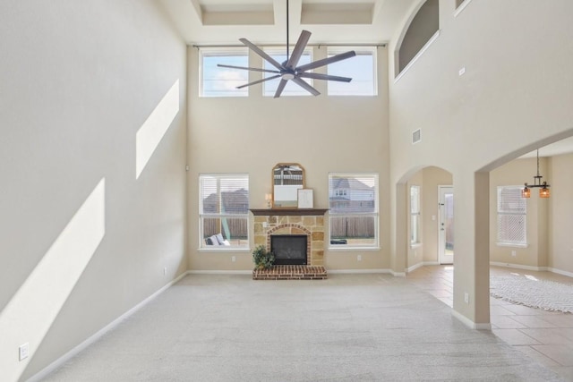 living room featuring a high ceiling, a stone fireplace, ceiling fan with notable chandelier, and light colored carpet