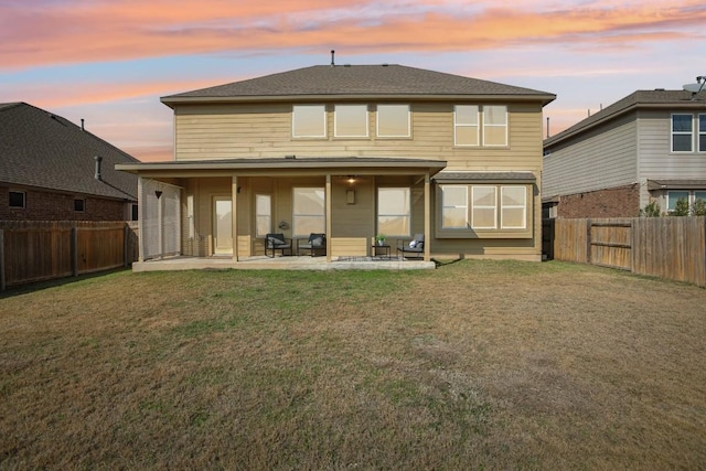 back house at dusk with a patio area and a lawn