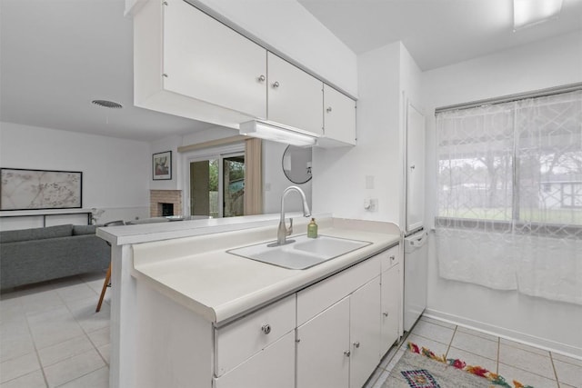 kitchen featuring light tile patterned flooring, a fireplace, sink, white cabinets, and kitchen peninsula