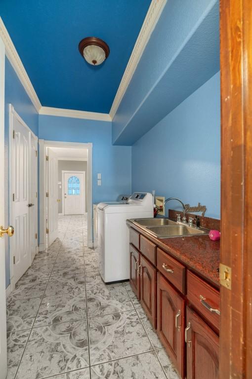 clothes washing area with cabinets, ornamental molding, sink, and washing machine and clothes dryer