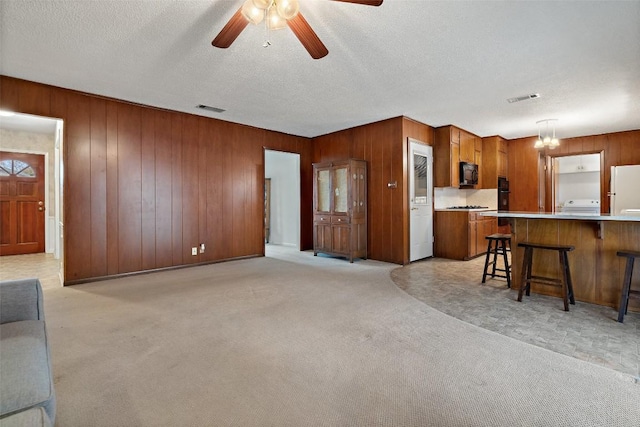 living room featuring wood walls, ceiling fan with notable chandelier, light carpet, and a textured ceiling