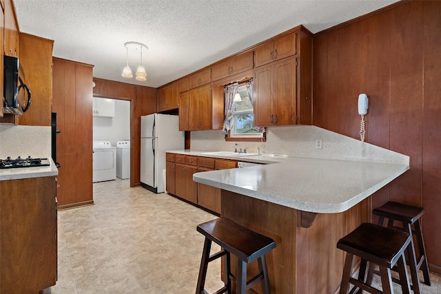 kitchen featuring a kitchen bar, decorative light fixtures, white refrigerator, kitchen peninsula, and independent washer and dryer