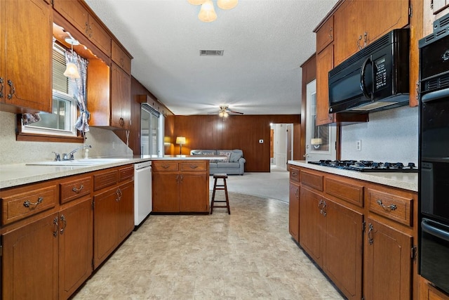 kitchen with sink, hanging light fixtures, a kitchen breakfast bar, ceiling fan, and black appliances