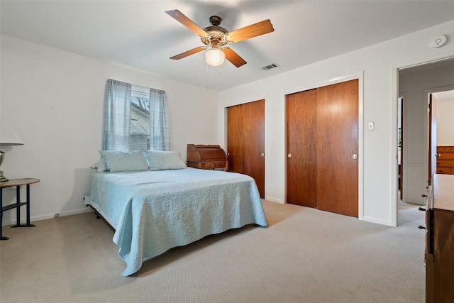 bedroom with multiple closets, light carpet, and ceiling fan