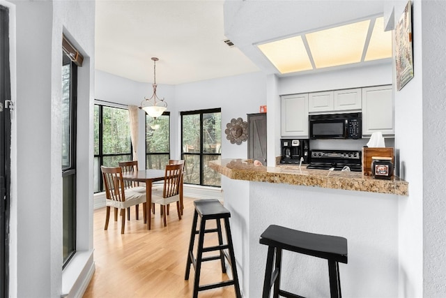 kitchen with black appliances, white cabinetry, kitchen peninsula, light stone countertops, and light wood-type flooring