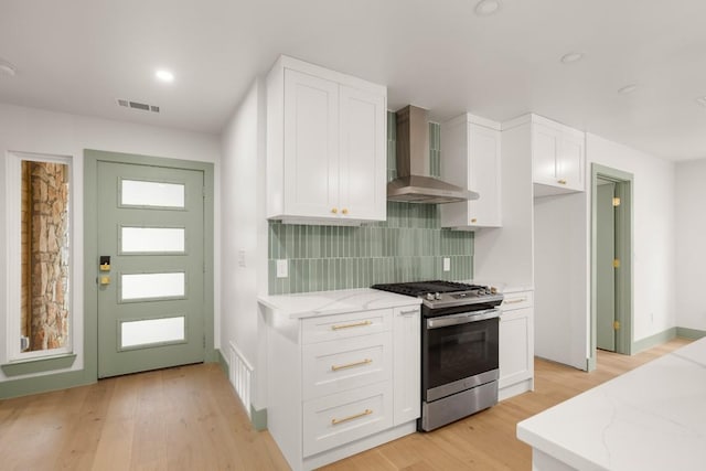 kitchen with gas stove, light stone counters, white cabinets, wall chimney range hood, and backsplash