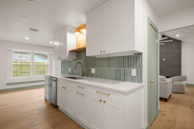 kitchen with sink, light hardwood / wood-style flooring, white cabinetry, backsplash, and stainless steel dishwasher