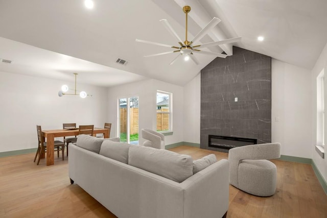 living room featuring a tiled fireplace, vaulted ceiling with beams, ceiling fan with notable chandelier, and light wood-type flooring