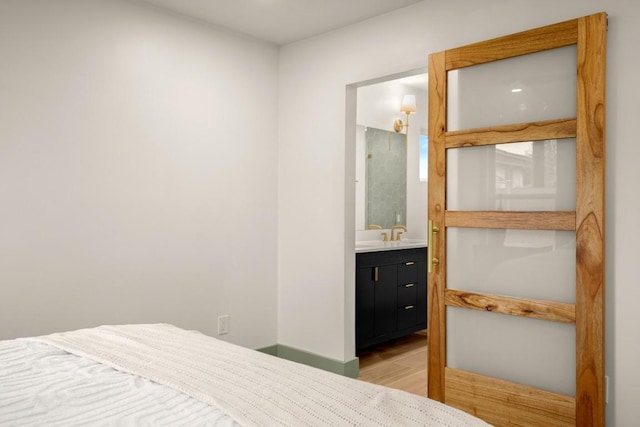 bedroom with ensuite bathroom, sink, and light hardwood / wood-style floors